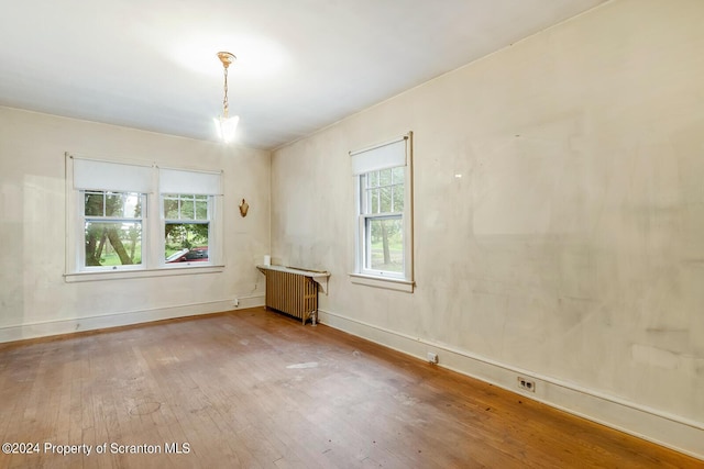 spare room with hardwood / wood-style flooring, plenty of natural light, radiator heating unit, and an inviting chandelier