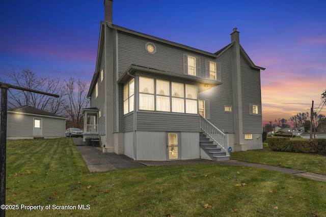 back house at dusk featuring a lawn and a patio