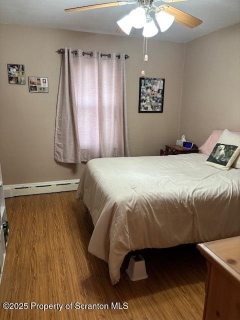 bedroom with a baseboard heating unit, baseboards, wood finished floors, and ceiling fan