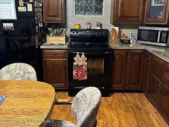 kitchen with light wood-style floors, glass insert cabinets, dark brown cabinetry, and black appliances