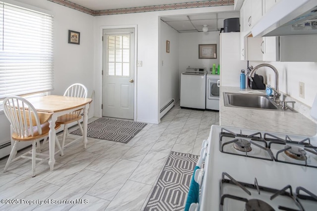 kitchen featuring washer and dryer, a sink, baseboard heating, under cabinet range hood, and light countertops