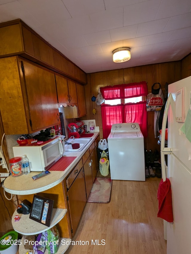 kitchen with white appliances, washer / clothes dryer, light hardwood / wood-style flooring, and sink