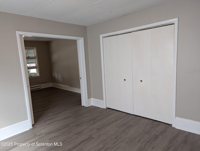 unfurnished bedroom featuring hardwood / wood-style flooring, a baseboard heating unit, and a closet