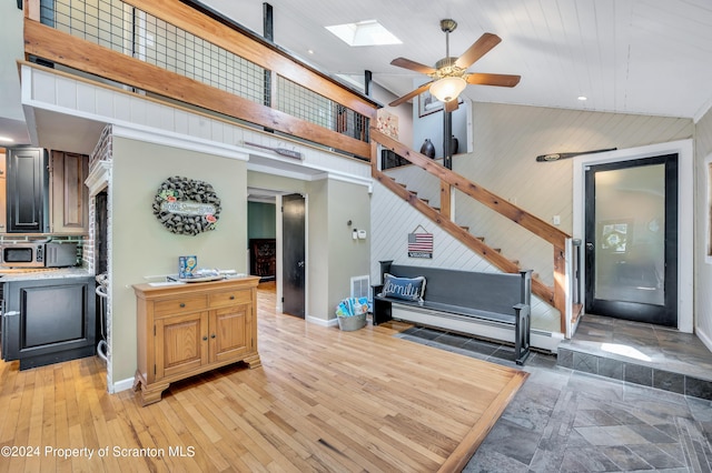 interior space featuring a skylight, ceiling fan, a baseboard heating unit, and wood walls