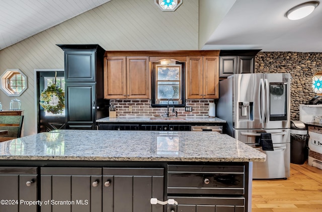 kitchen with stainless steel refrigerator with ice dispenser, lofted ceiling, light stone counters, and a kitchen island