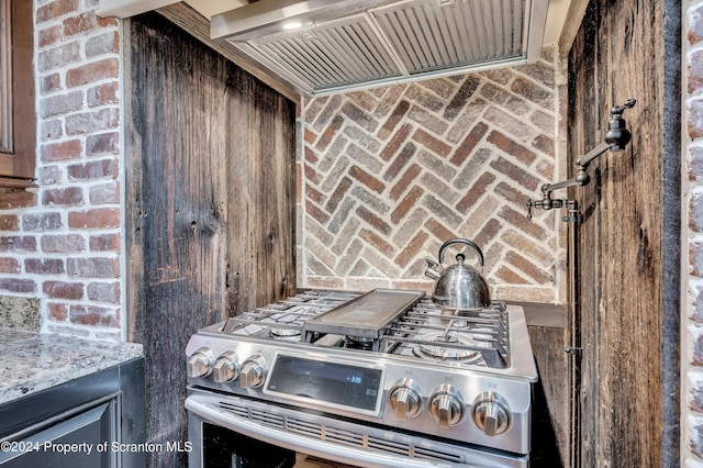 kitchen with ventilation hood, dark brown cabinets, light stone counters, and range