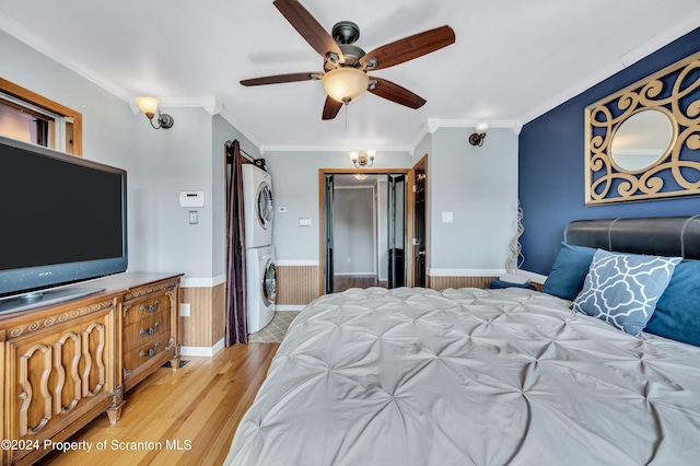 bedroom featuring wood walls, stacked washer and clothes dryer, light hardwood / wood-style flooring, ceiling fan, and a closet