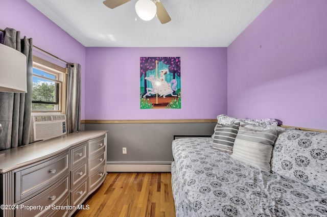 bedroom with light wood-type flooring, a textured ceiling, baseboard heating, cooling unit, and ceiling fan