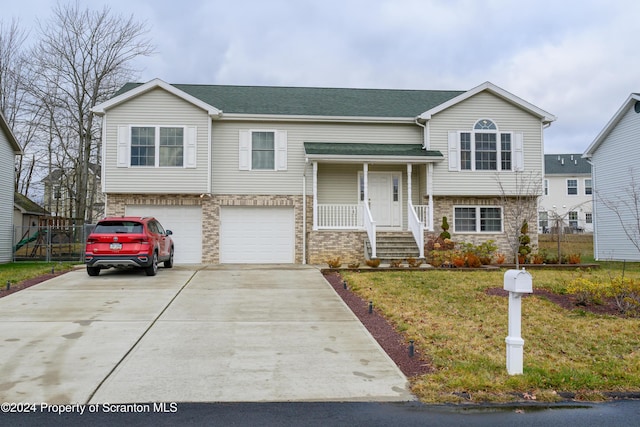 raised ranch with covered porch, a garage, and a front lawn