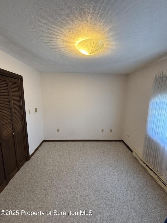 unfurnished bedroom with baseboards, carpet flooring, a closet, and a baseboard heating unit