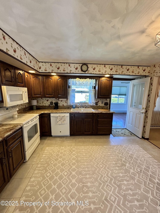 kitchen with a sink, white appliances, light stone counters, wallpapered walls, and dark brown cabinets
