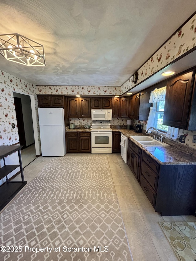 kitchen featuring wallpapered walls, dark brown cabinets, a sink, and white appliances