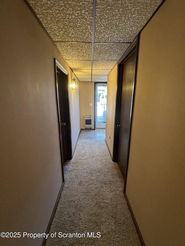 hall featuring baseboards, heating unit, and light colored carpet