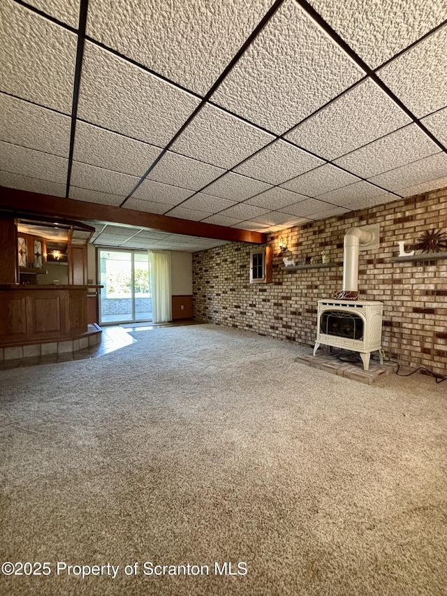 unfurnished living room featuring heating unit, a paneled ceiling, carpet floors, brick wall, and a wood stove