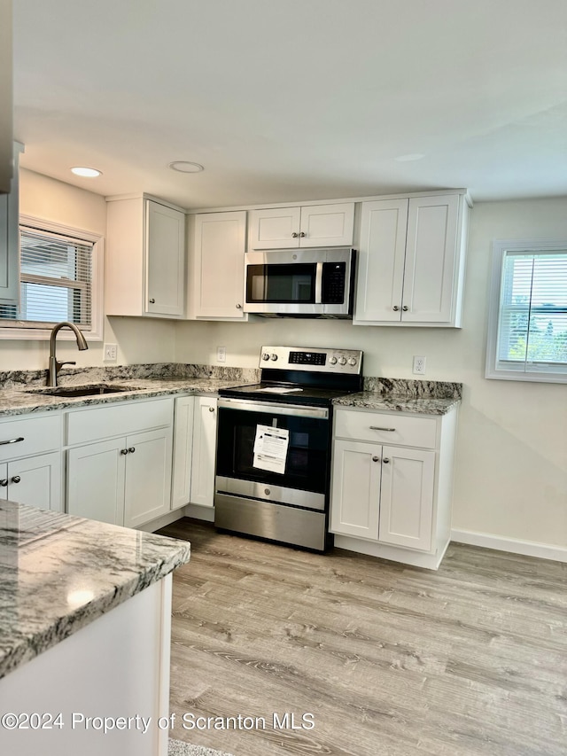 kitchen with sink, appliances with stainless steel finishes, light stone counters, white cabinets, and light wood-type flooring