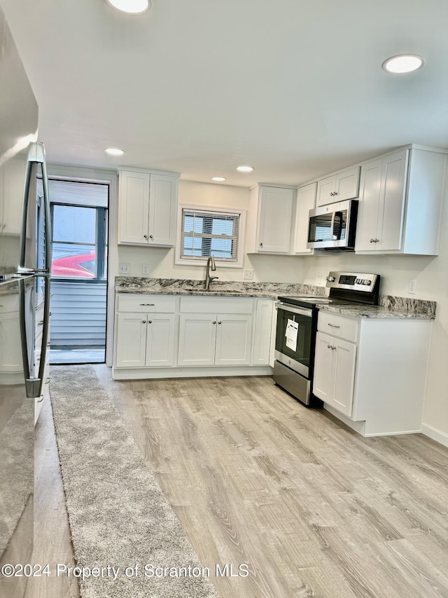 kitchen featuring white cabinetry, stainless steel appliances, sink, and light wood-type flooring