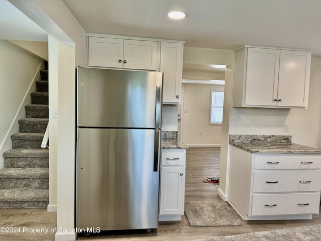 kitchen with stainless steel refrigerator, light wood-type flooring, light stone counters, and white cabinets