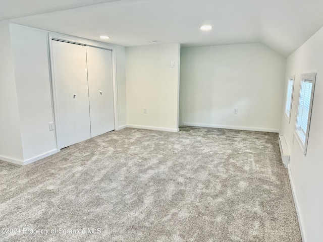 unfurnished bedroom featuring a baseboard radiator, carpet flooring, vaulted ceiling, and a closet