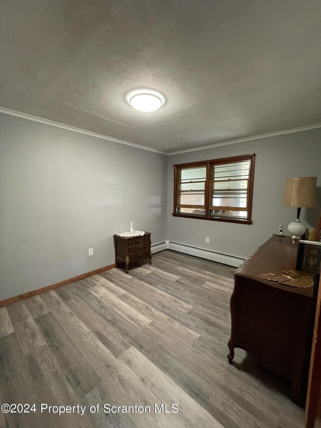 interior space with baseboard heating, hardwood / wood-style floors, a textured ceiling, and ornamental molding