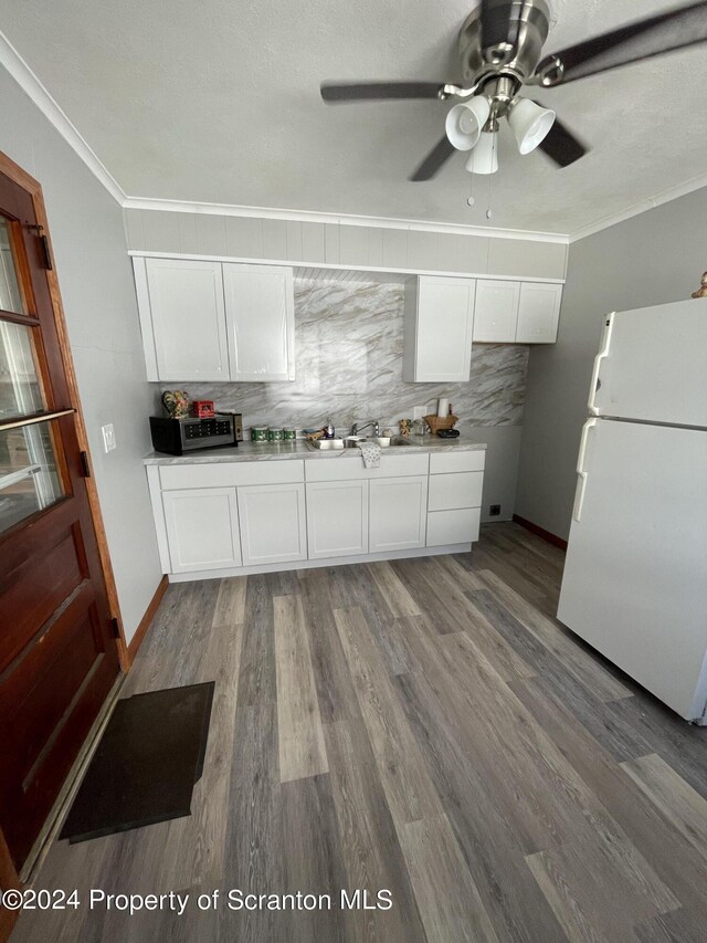 kitchen with backsplash, crown molding, wood-type flooring, white fridge, and white cabinetry