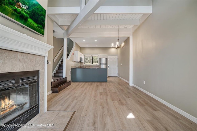 134 Laurel Hill Dr Unit 102, Greentown, PA 18426 - unfurnished living room with a tiled fireplace, beam ceiling, light wood-style floors, a chandelier, and stairway