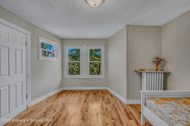 252 River St, Forty Fort, PA 18704 - unfurnished bedroom featuring radiator, light wood finished floors, and a textured ceiling