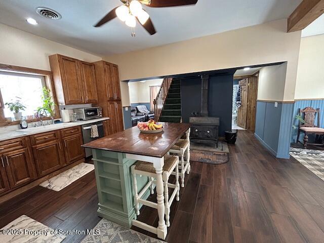 kitchen with dark wood-type flooring, sink, a wood stove, stainless steel dishwasher, and ceiling fan