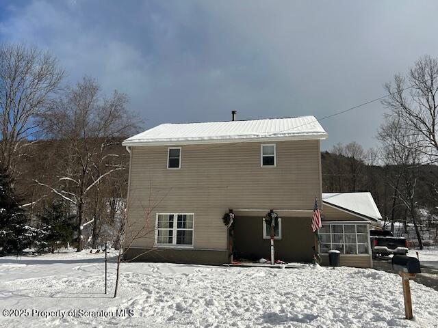 snow covered back of property featuring a sunroom