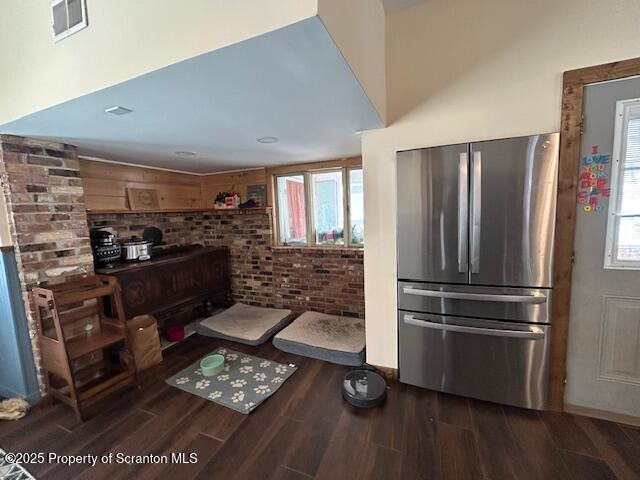 kitchen with brick wall, wood-type flooring, and stainless steel fridge