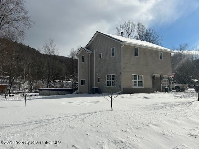 snow covered back of property featuring central AC