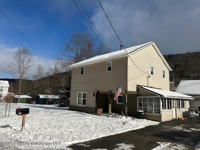 snow covered rear of property featuring a sunroom