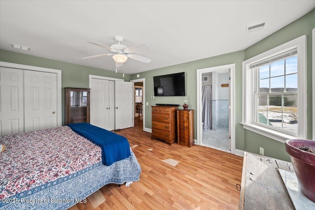 bedroom with hardwood / wood-style flooring, multiple closets, ensuite bath, and ceiling fan