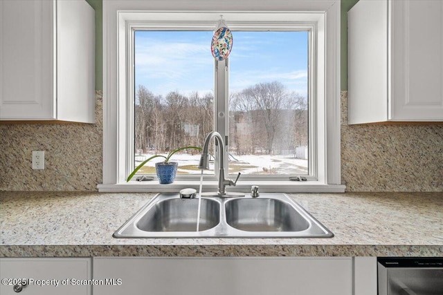 kitchen featuring stainless steel dishwasher, sink, white cabinetry, and tasteful backsplash