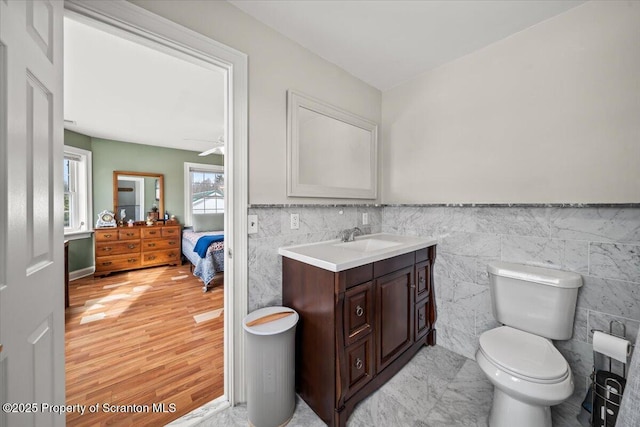 bathroom with wood-type flooring, toilet, tile walls, ceiling fan, and vanity