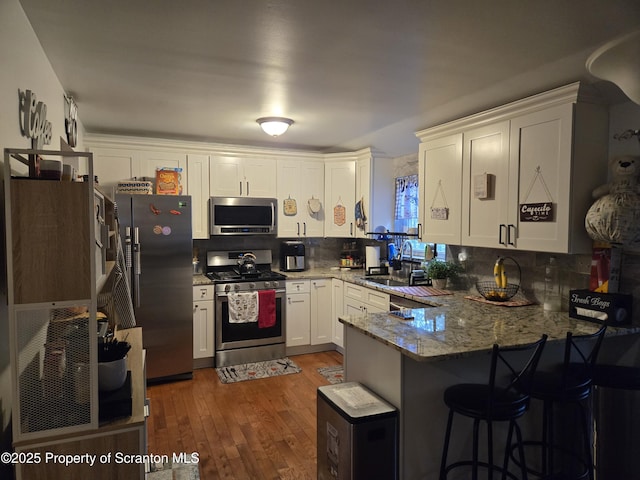 kitchen featuring sink, decorative backsplash, dark hardwood / wood-style flooring, kitchen peninsula, and stainless steel appliances