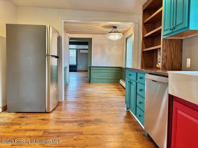 kitchen with an inviting chandelier, hanging light fixtures, light wood-type flooring, a baseboard radiator, and appliances with stainless steel finishes