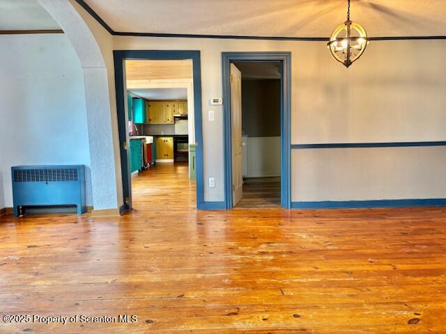 spare room with ornamental molding, an inviting chandelier, and light wood-type flooring