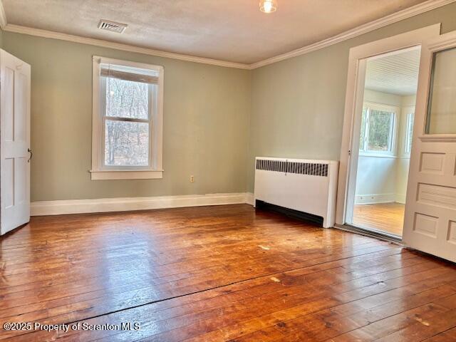 spare room with wood-type flooring, ornamental molding, radiator heating unit, and a wealth of natural light