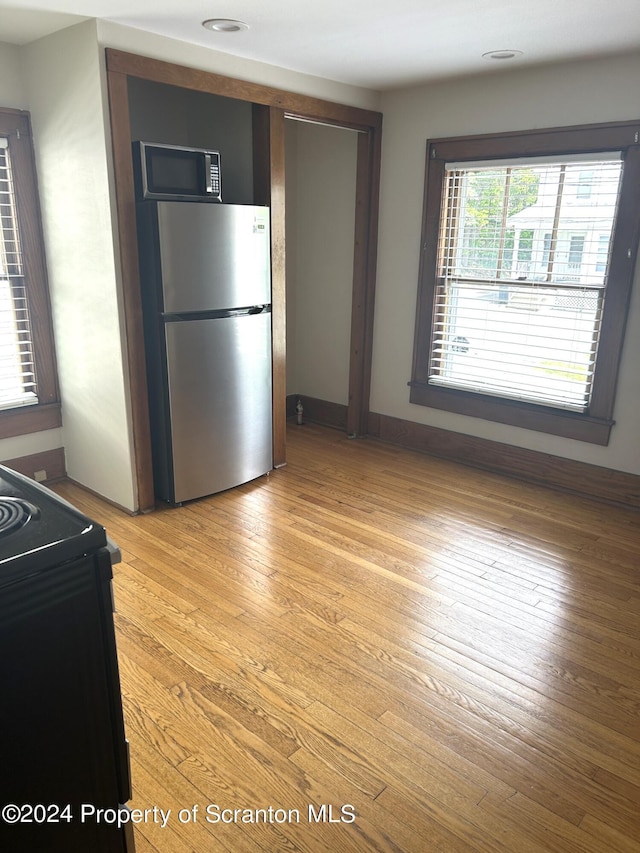 kitchen with black range with electric stovetop, stainless steel fridge, and light wood-type flooring