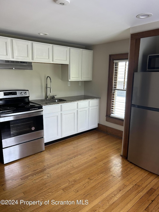 kitchen featuring appliances with stainless steel finishes, sink, dark stone countertops, light hardwood / wood-style floors, and white cabinetry