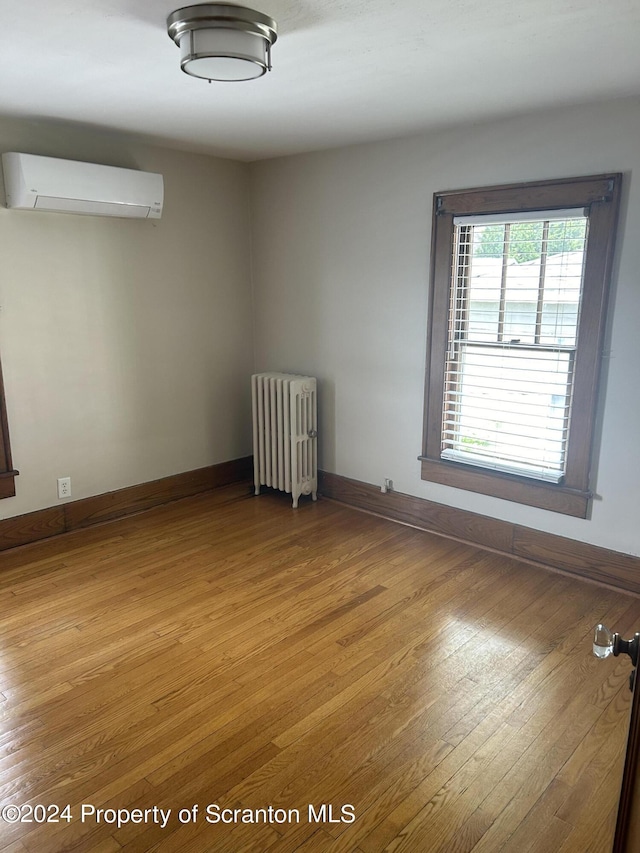 spare room featuring radiator heating unit, a wall unit AC, and light hardwood / wood-style flooring