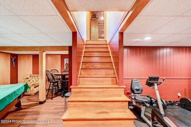 stairway featuring a paneled ceiling, wood walls, hardwood / wood-style floors, and pool table