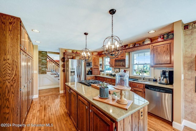 kitchen featuring a center island, light wood-type flooring, decorative light fixtures, light stone counters, and stainless steel appliances