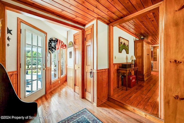 doorway with wood walls, light wood-type flooring, wooden ceiling, and vaulted ceiling