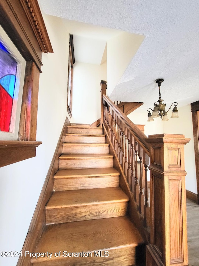 stairs featuring wood-type flooring, a textured ceiling, and a notable chandelier