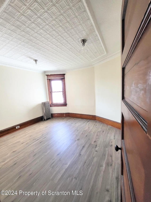 empty room featuring radiator heating unit, wood-type flooring, and ornamental molding