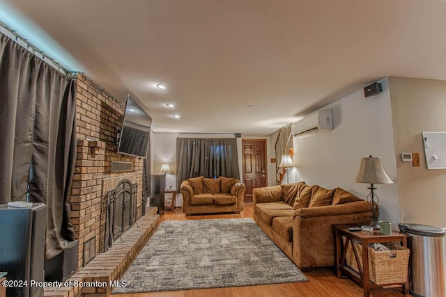 living room with a wall mounted AC, wood-type flooring, and a brick fireplace