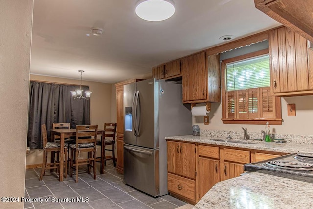 kitchen with an inviting chandelier, sink, stainless steel refrigerator with ice dispenser, decorative light fixtures, and light stone counters