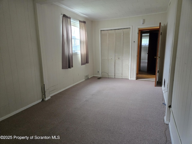 unfurnished bedroom featuring carpet flooring, crown molding, wood walls, a closet, and baseboards