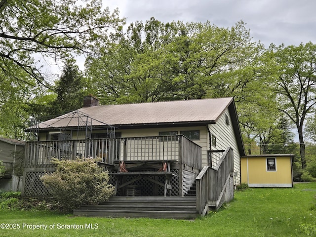 back of property featuring a lawn, a wooden deck, a chimney, and an outdoor structure